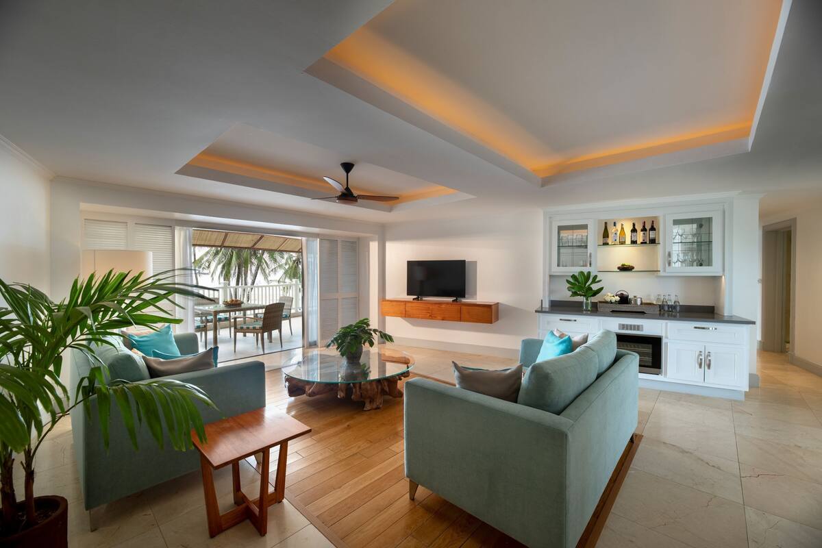 Una sala de estar moderna con una mesa de centro de vidrio, dos sofás, un televisor y una zona de cocina con armarios y una encimera.