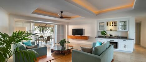 A modern living room with a glass coffee table, two sofas, a TV, and a kitchen area with cabinets and a countertop.