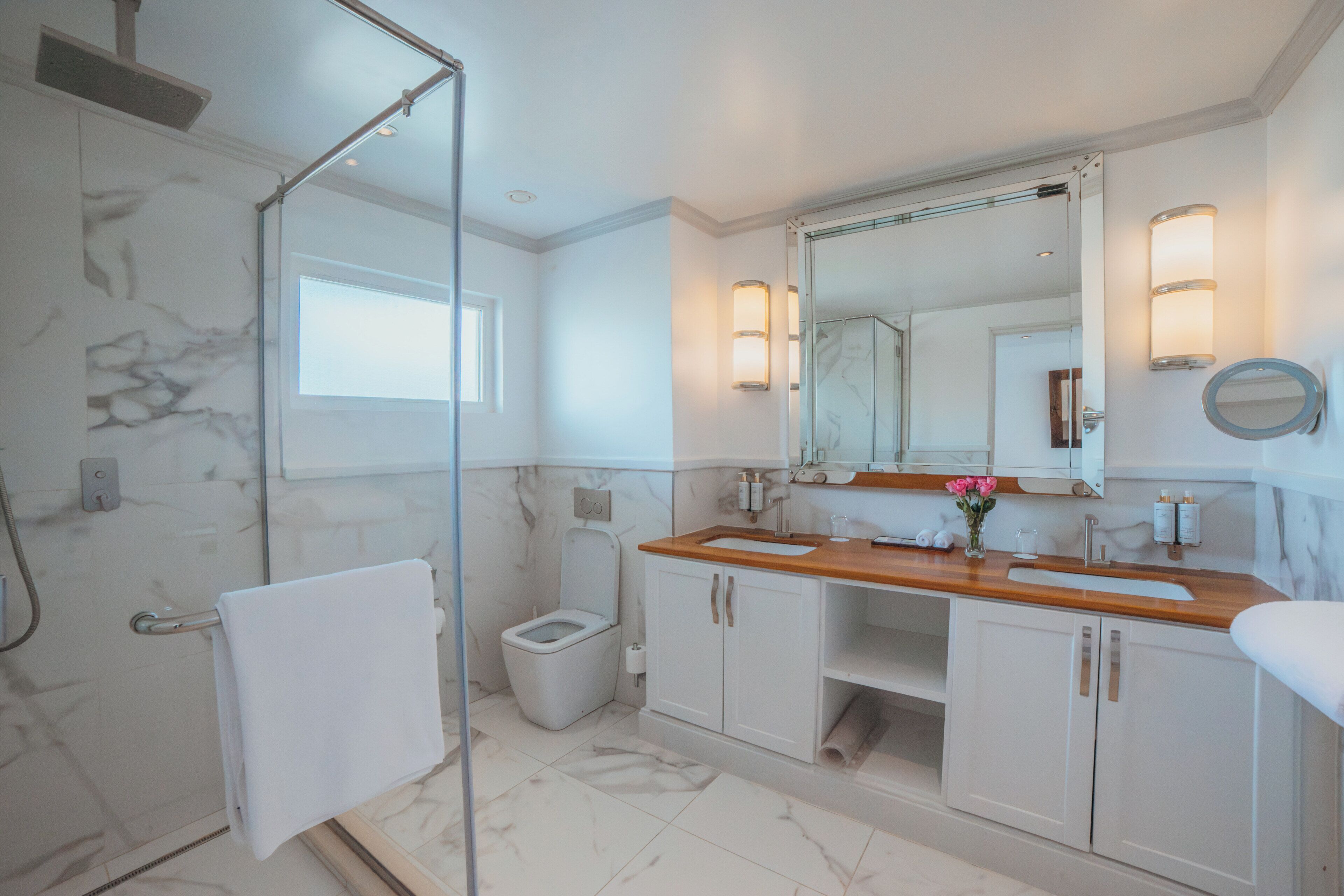 A modern bathroom with a glass shower enclosure, a toilet, a sink with a wooden countertop, and a large mirror.