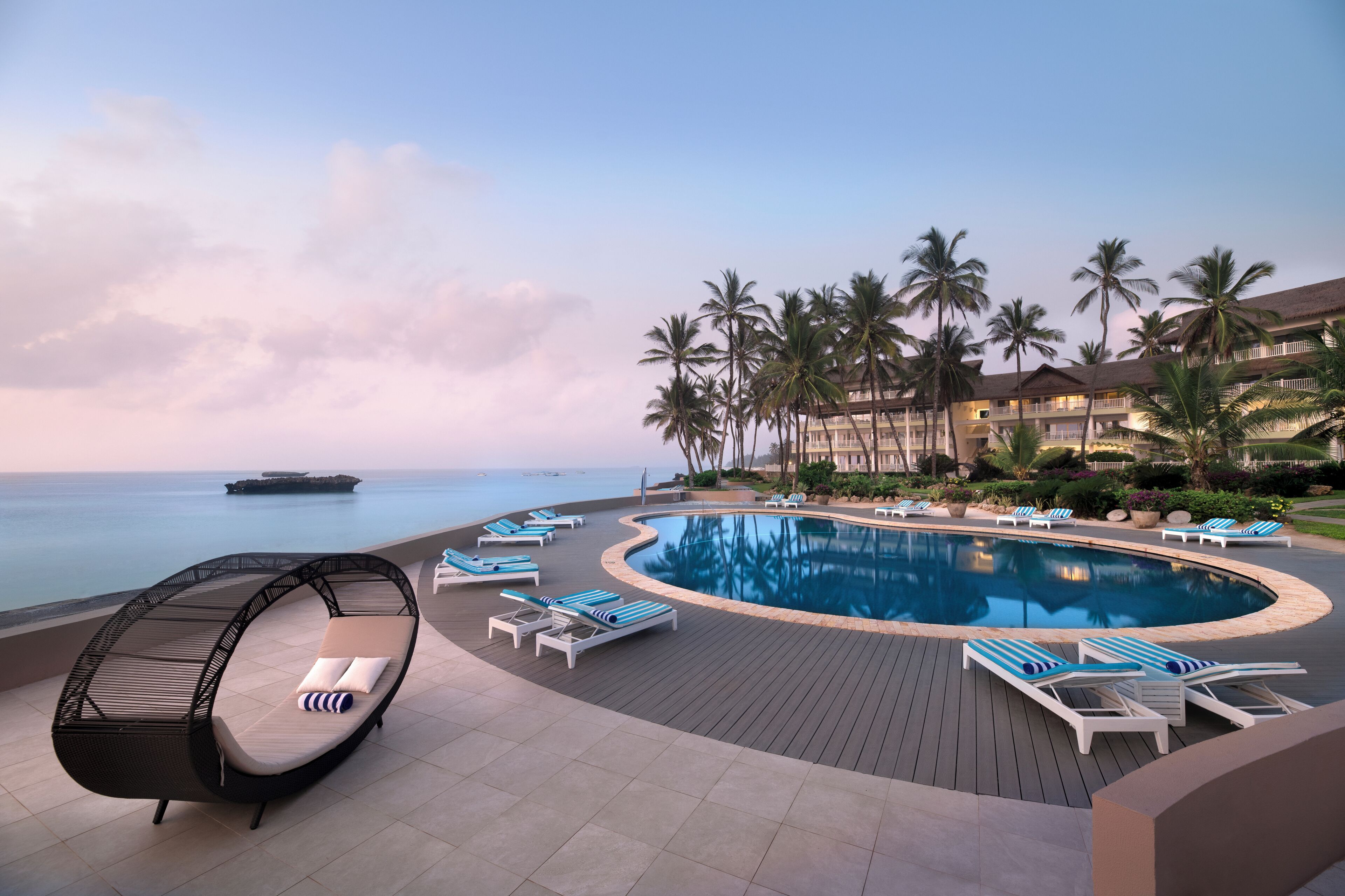 A poolside area with lounge chairs, a hanging chair, and palm trees.