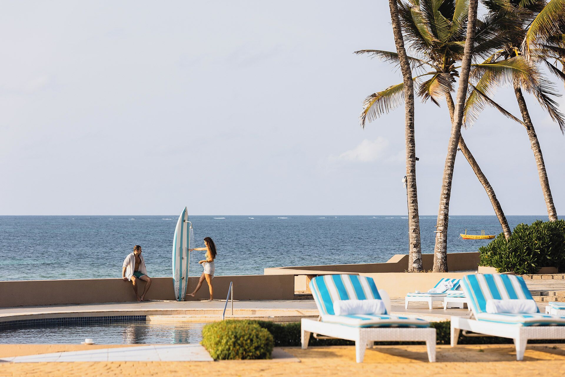 A poolside area with lounge chairs, a pool, and a view of the ocean.