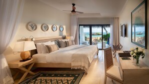 Habitación de hotel con cama, escritorio, silla, televisión, ventilador de techo y vista al océano.
