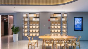 A modern conference room with a round wooden table and chairs, surrounded by bookshelves with illuminated shelves. - JI Hotel (Shenzhen)