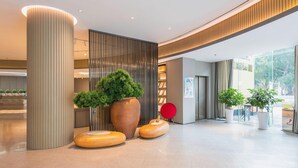 A modern lobby with a large cylindrical column, a tall potted plant, and a red circular object. - JI Hotel (Shenzhen)