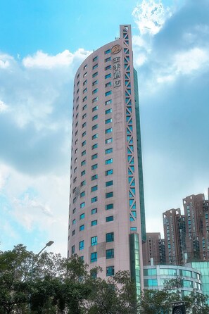 A tall, modern building with a curved facade, multiple windows, and a prominent logo at the top. - JI Hotel (Shenzhen)