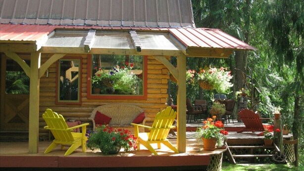 Eine Holzhütte mit Veranda, gelben Adirondack-Stühlen und Kübelpflanzen.
