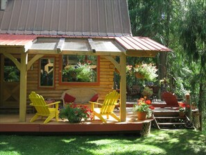 Une cabane en bois dotée d’un porche, de chaises Adirondack jaunes et de plantes en pot.