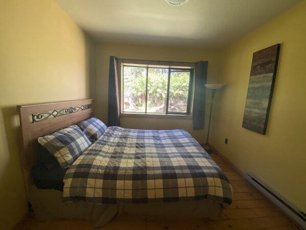 Une chambre à coucher avec un lit, une fenêtre avec des rideaux, une lampe et un tableau accroché au mur.