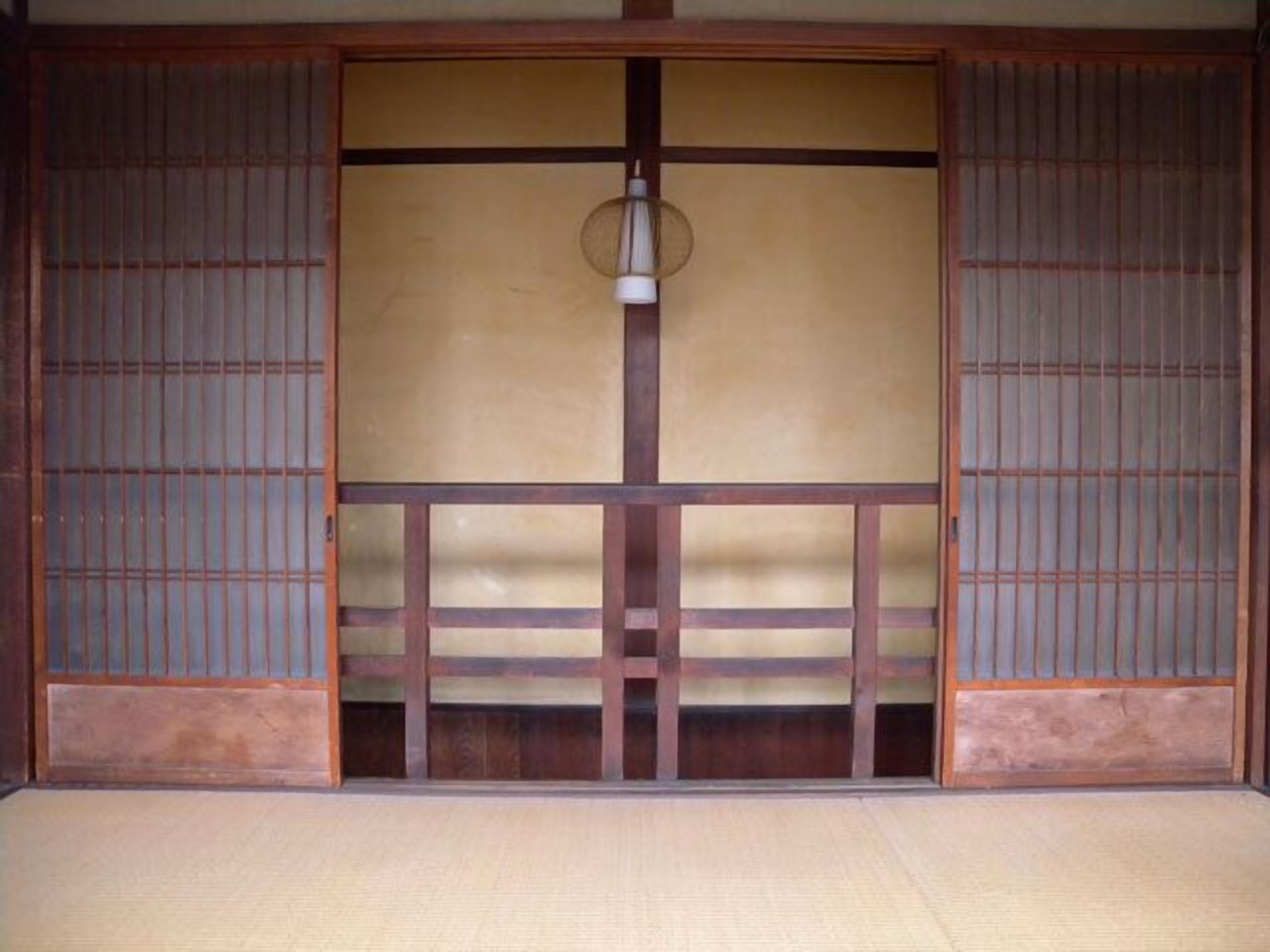 Una habitación tradicional japonesa con suelo de tatami, puertas correderas y una lámpara colgante.