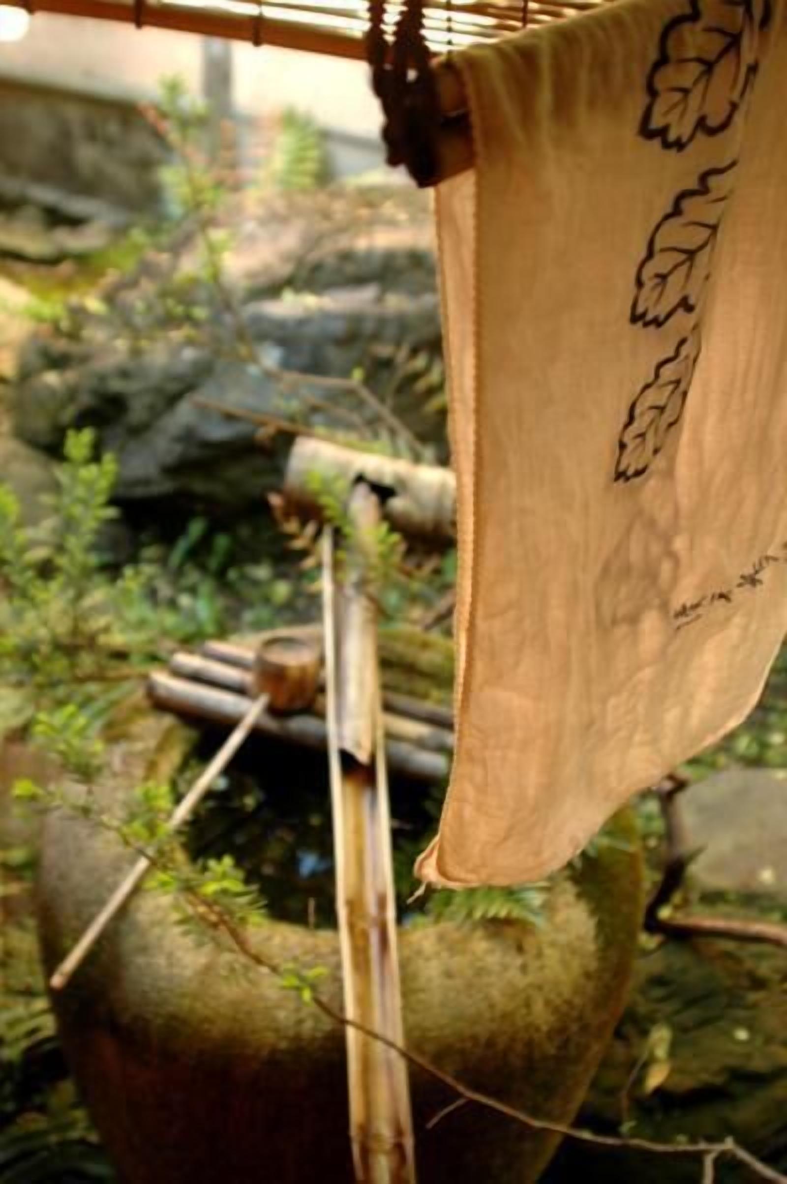 Estructura de bambú con un tejido colgante, posiblemente un objeto tradicional o cultural, en un entorno natural con rocas y follaje.