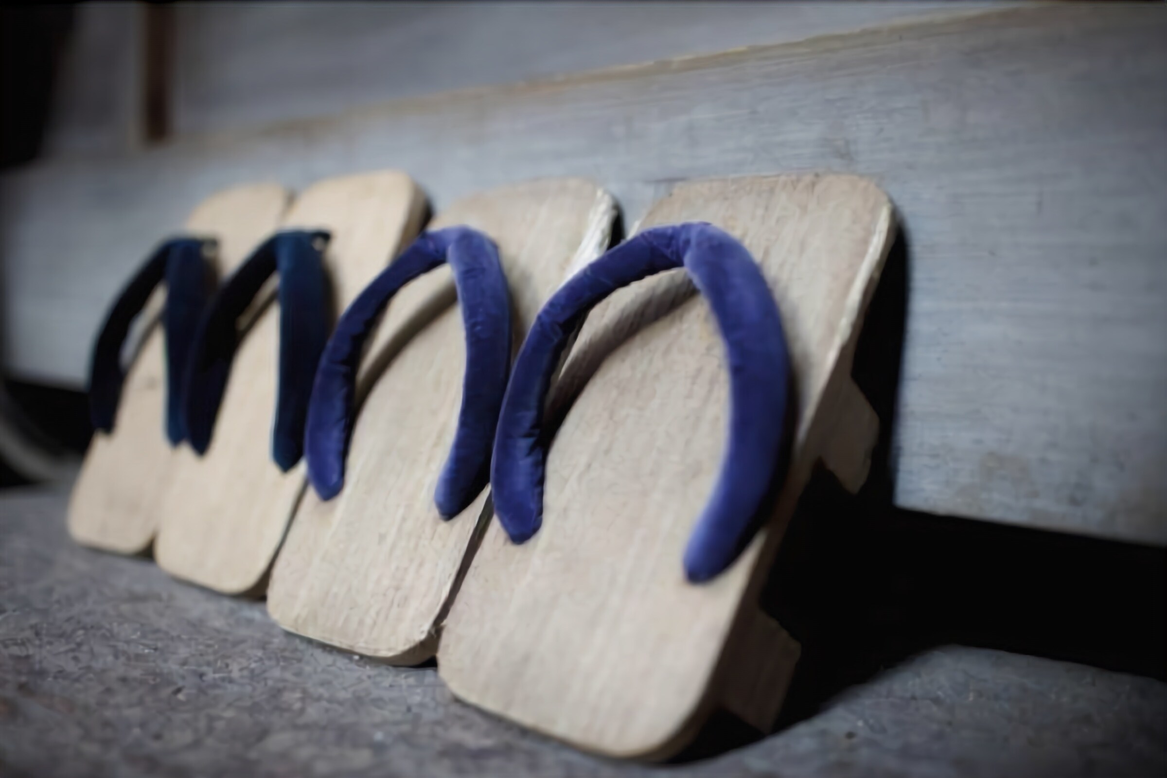 A row of wooden flip-flops with blue straps on a wooden bench.