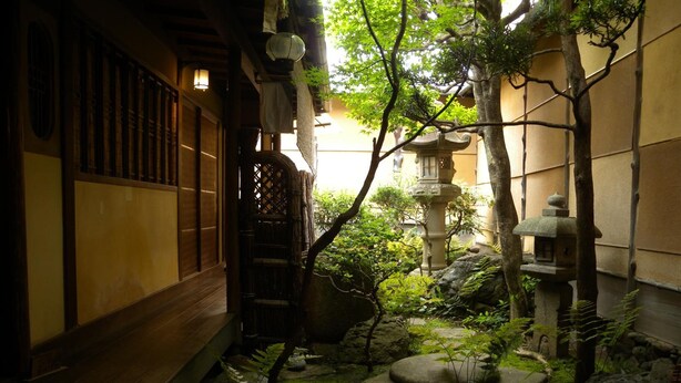 Un jardín japonés tradicional con un sendero de madera, faroles de piedra y un pequeño estanque.