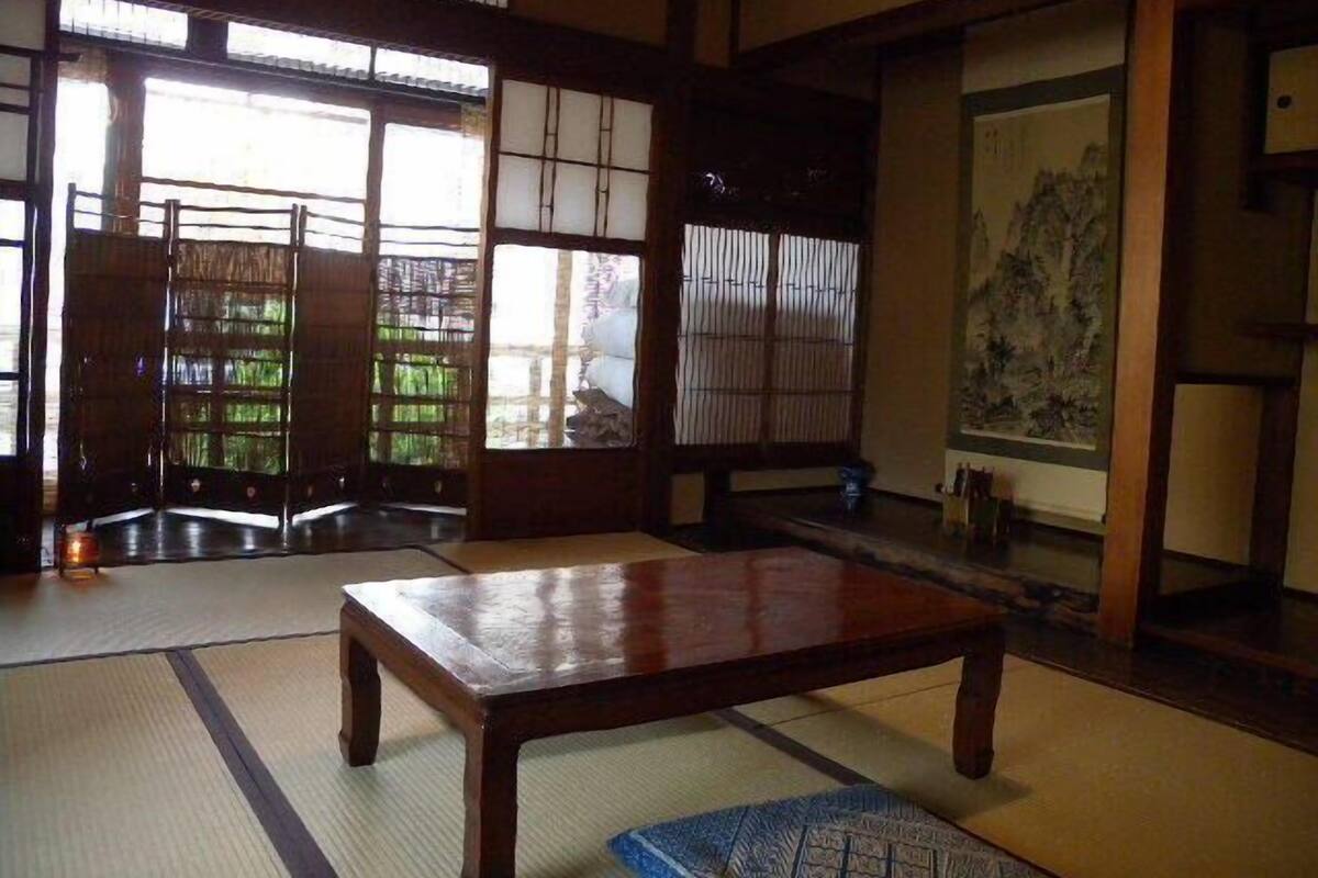 Een traditionele Japanse kamer met tatami vloeren, een houten tafel, schuifdeuren en een schilderij aan de muur.