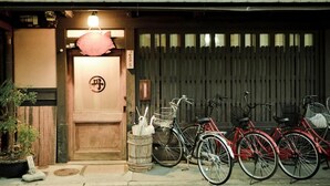 Una entrada tradicional japonesa con puerta de madera, un letrero con caracteres japoneses y bicicletas estacionadas afuera.