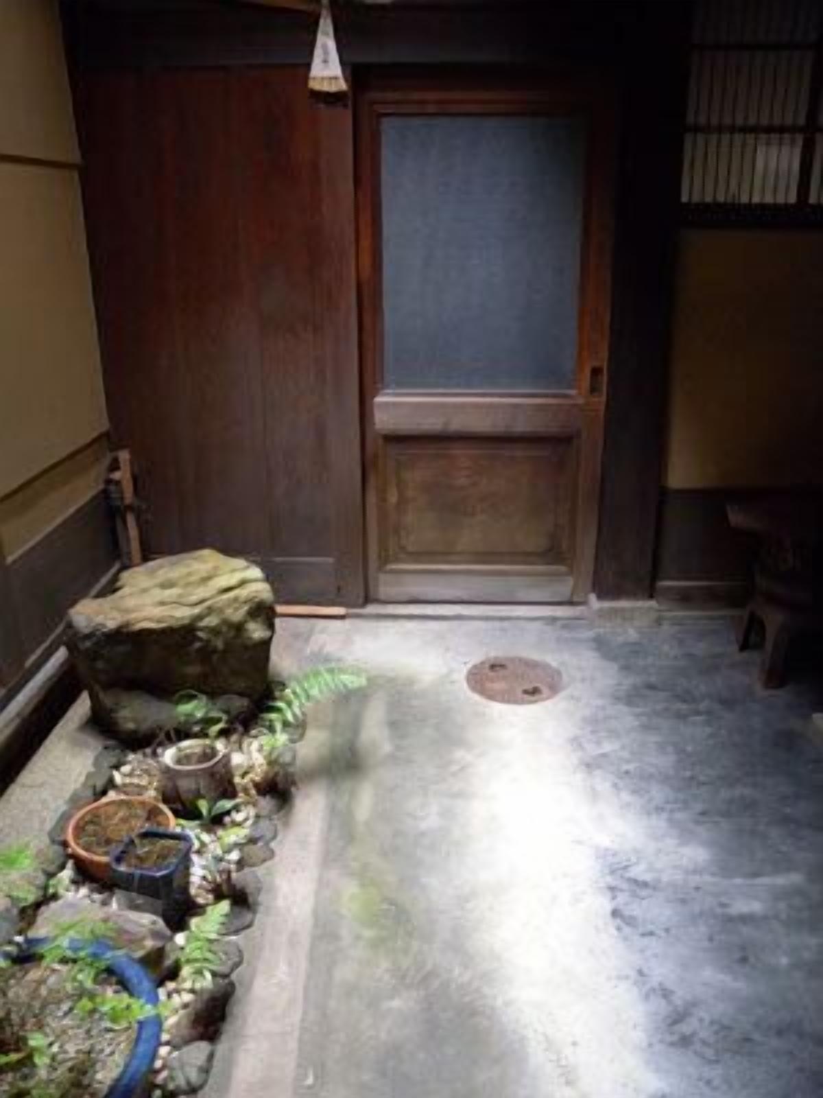 A traditional Japanese room with tatami flooring, a shoji screen door, and a small rock garden with plants and a water feature.