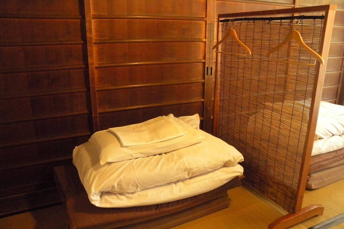 Een net opgemaakt bed met witte lakens in een kamer met houten lambrisering en een deur van bamboe.