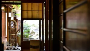Una habitación japonesa tradicional con suelo de tatami, puerta corredera de shoji y vistas a la vegetación exterior.
