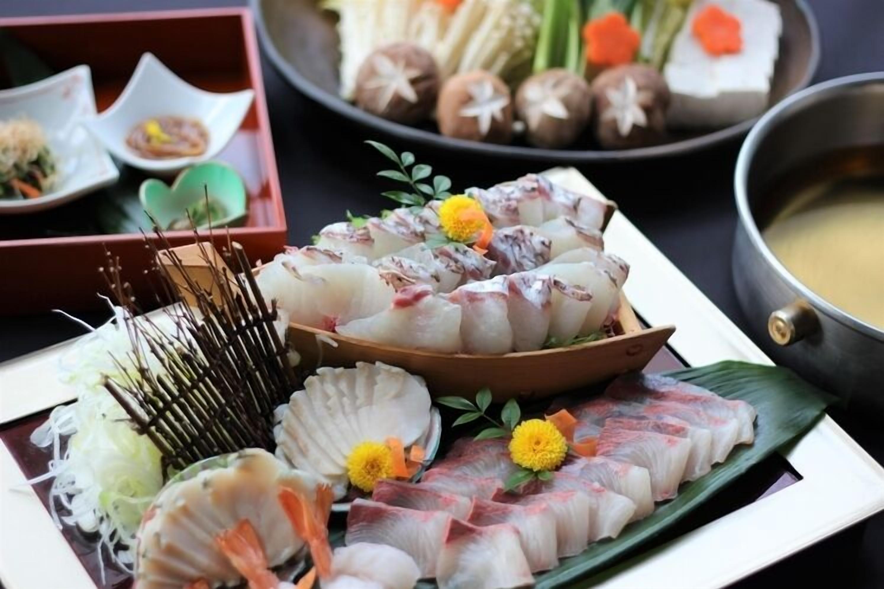 A variety of seafood dishes, including sashimi and sushi, arranged on a table with a bowl of soup and other side dishes.