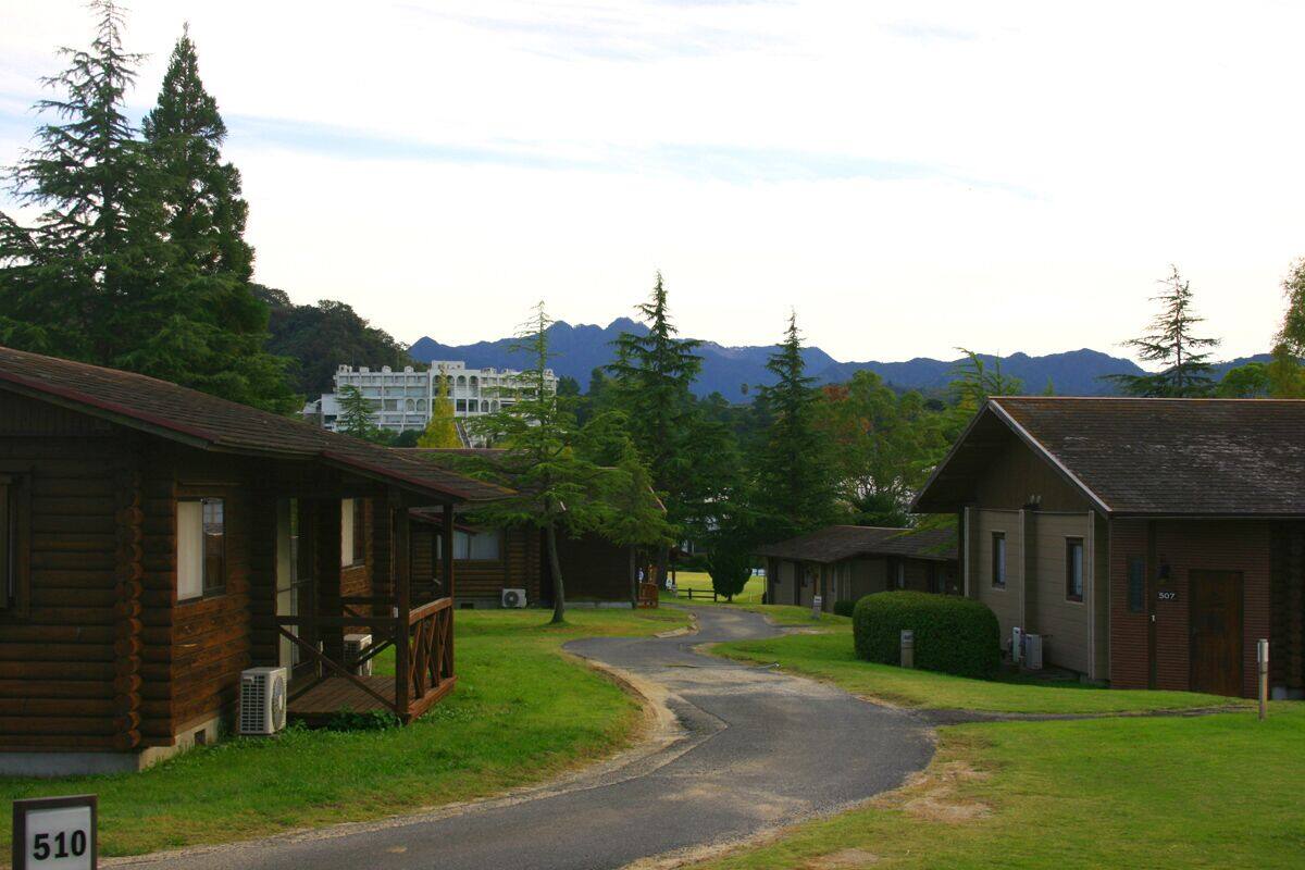 A rustic lodge with a wooden exterior, a paved driveway, and a view of mountains in the background.