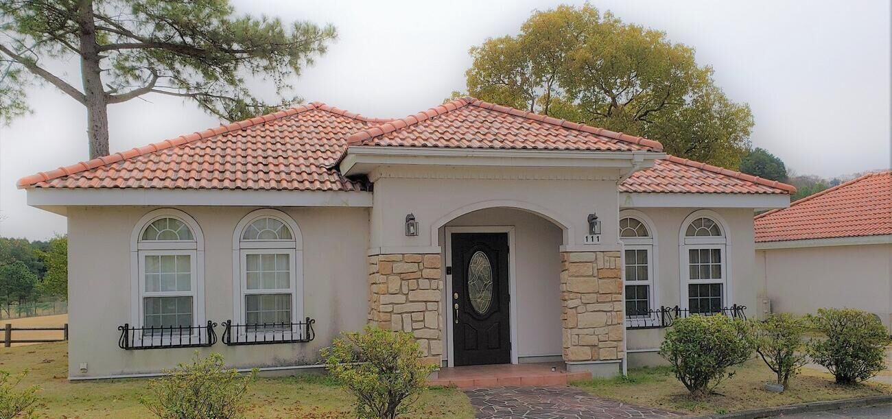 A single-story house with a tiled roof, stone facade, and a black front door.