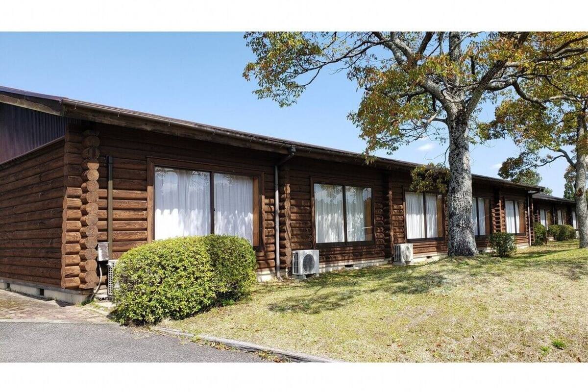 A row of log cabins with large windows, air conditioning units, and a well-maintained lawn.