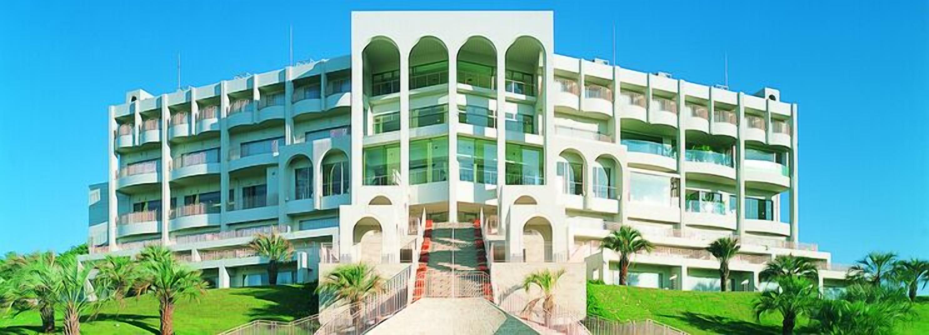 Un hotel de varios pisos con un patio central, balcones y palmeras.