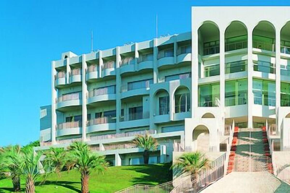 A multi-story hotel with a central courtyard, balconies, and palm trees.