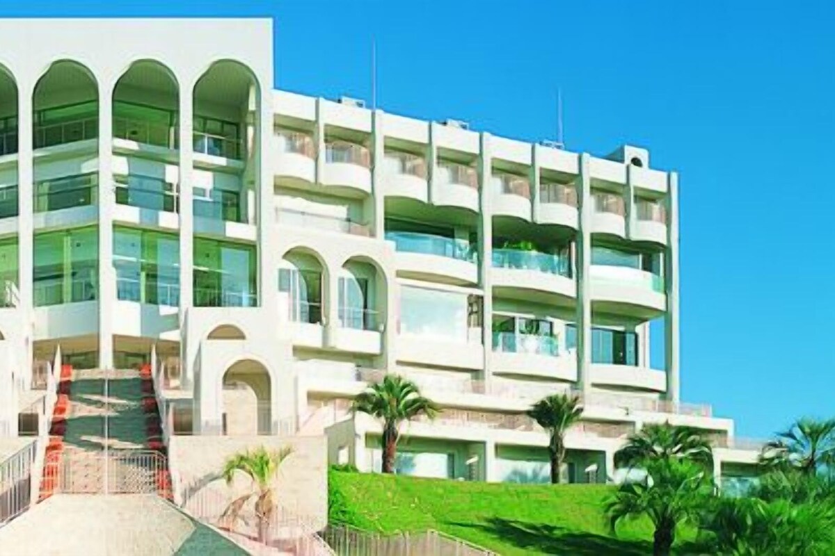 Un hotel de varios pisos con un patio central, balcones y palmeras.