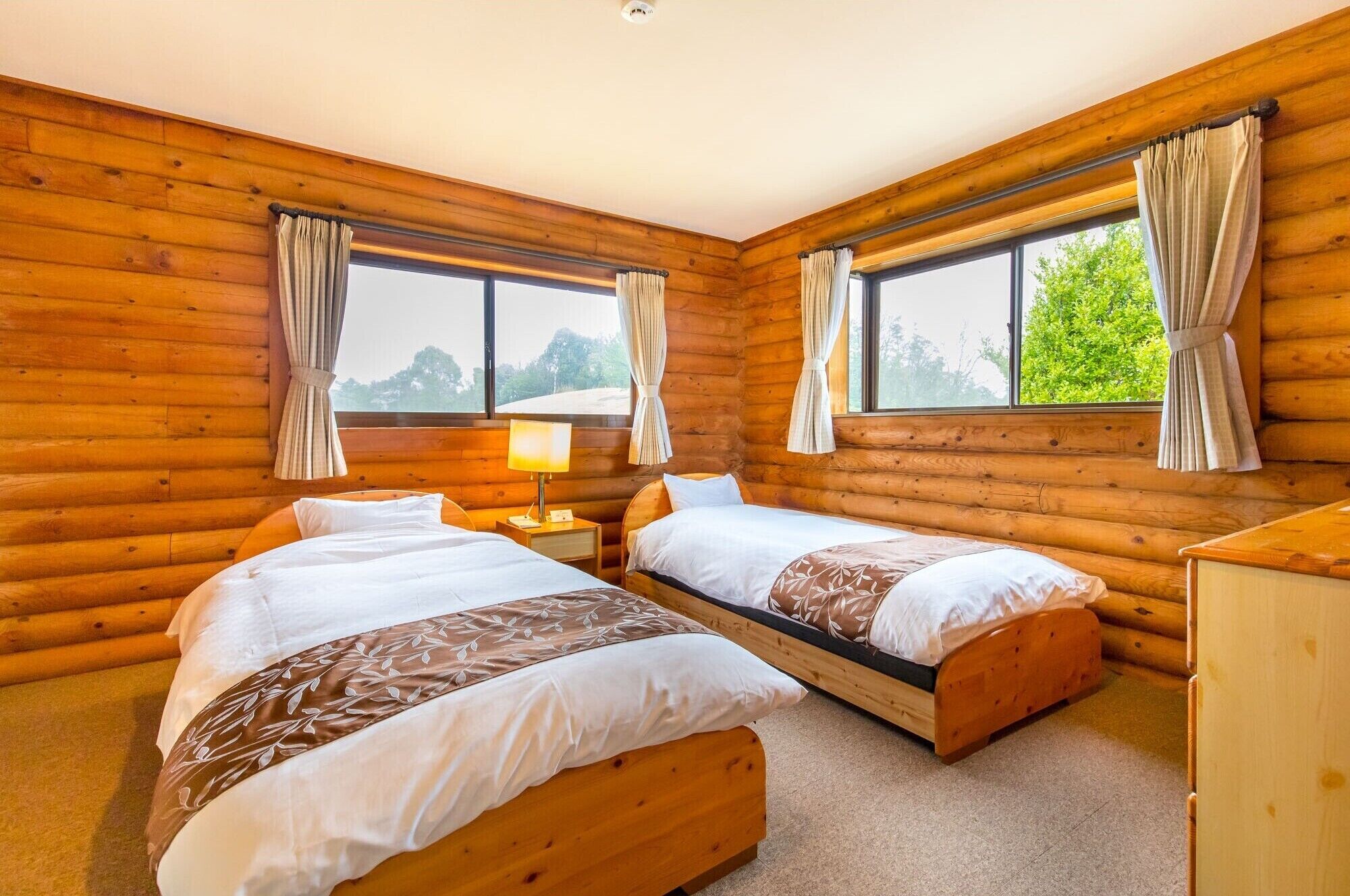 A log cabin bedroom with two beds, a nightstand, a lamp, and a dresser.