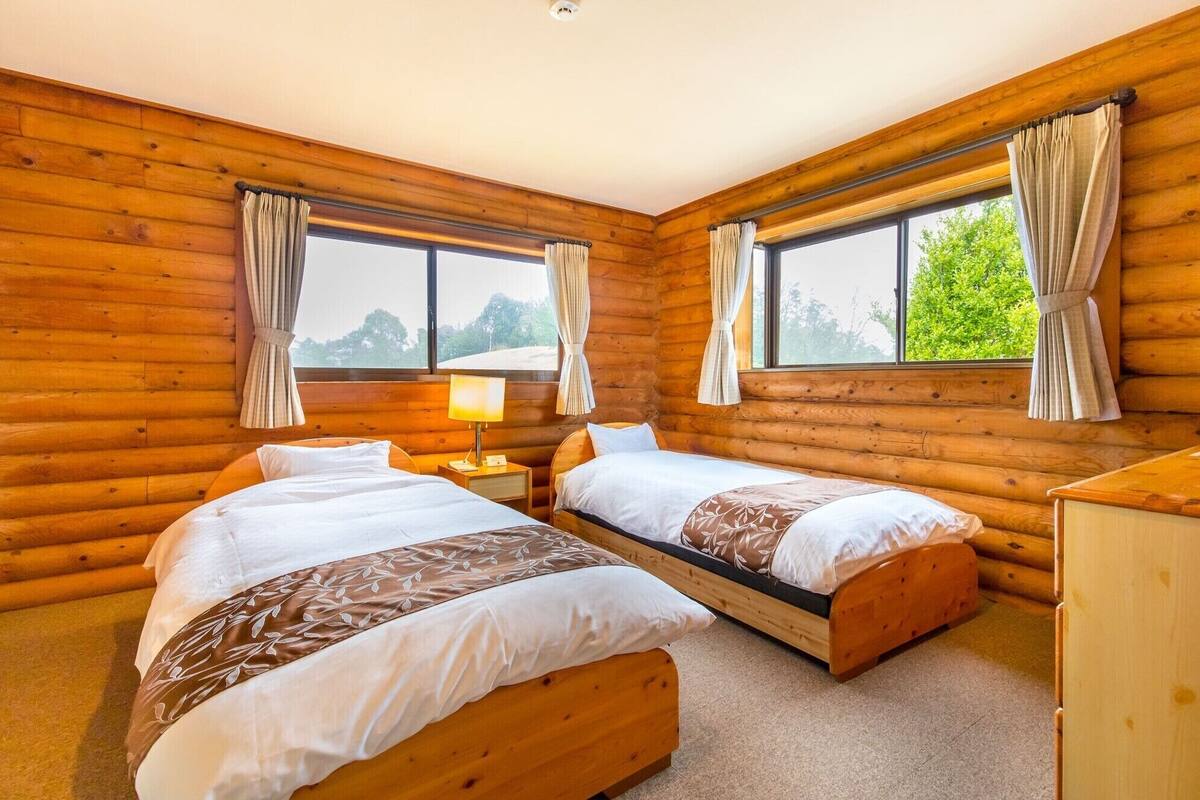 A log cabin bedroom with two beds, a nightstand, a lamp, and a dresser.