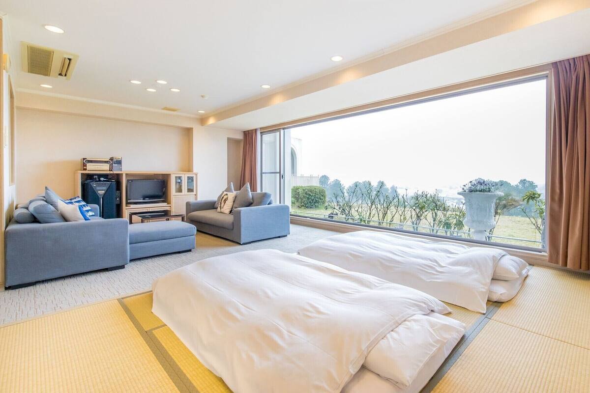 A hotel room with a bed, a sofa, a TV, and a large window with a view.
