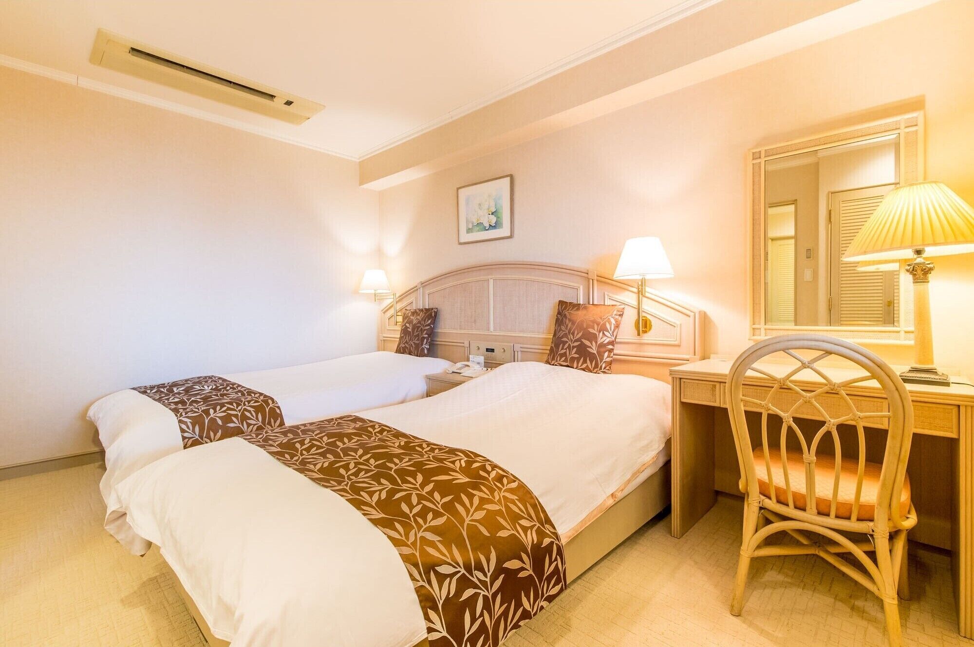 A hotel room with two beds, a desk, a chair, a lamp, and a mirror.
