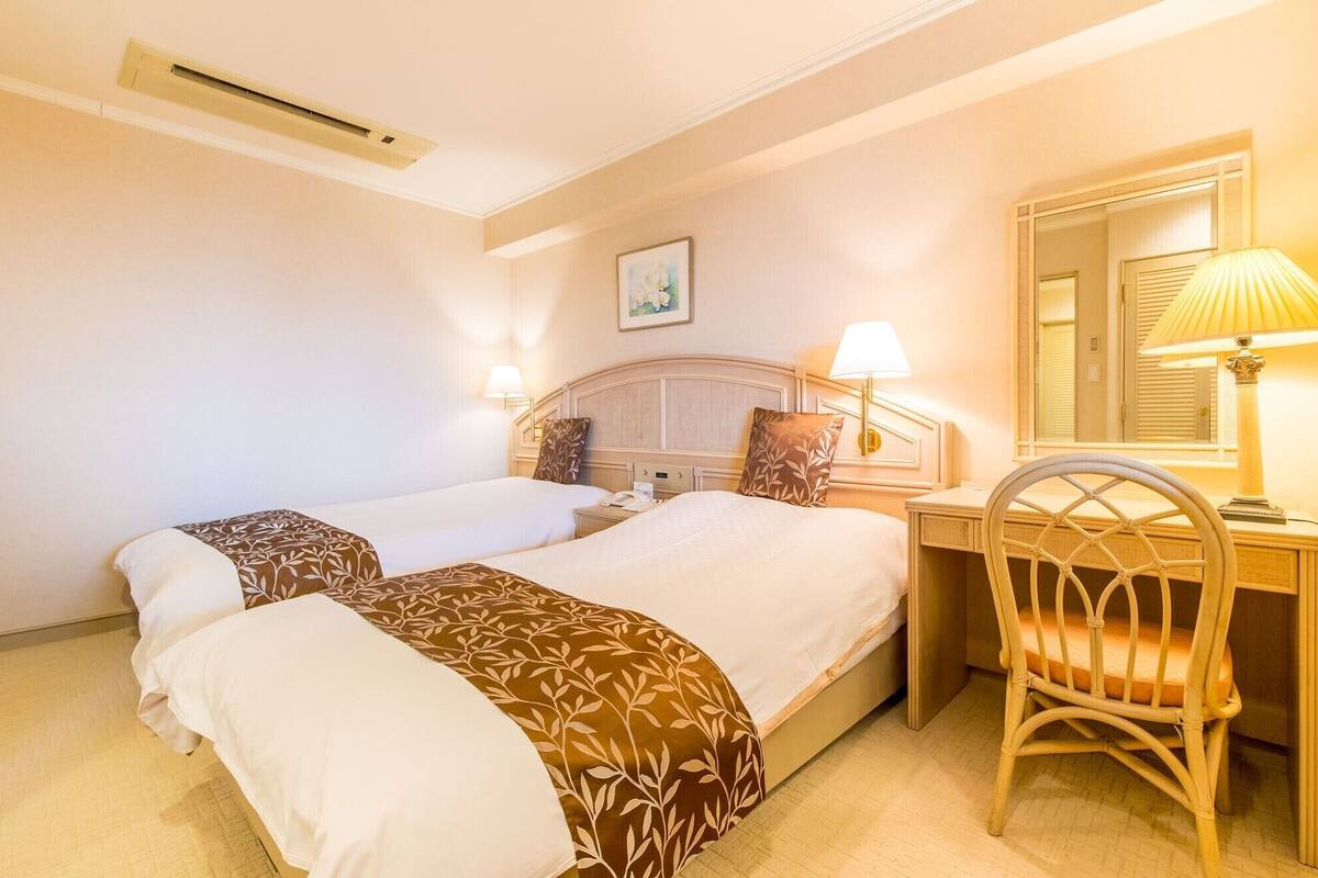 A hotel room with two beds, a desk, a chair, a lamp, and a mirror.