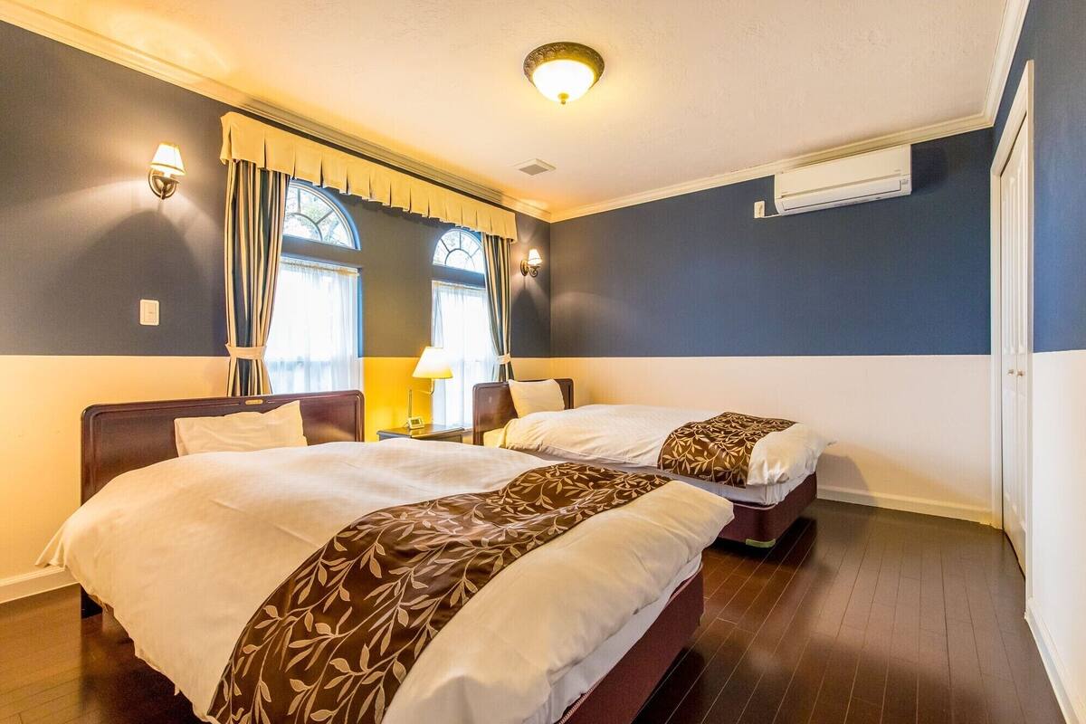 A hotel room with two beds, a window with curtains, a wall-mounted air conditioner, and a ceiling light.