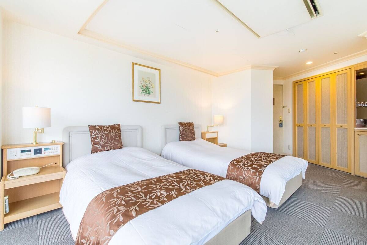A hotel room with two beds, bedside tables with lamps, a clock, a framed picture on the wall, and a wardrobe with a mirror.