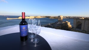 Une bouteille de vin et deux verres sur une table, avec vue sur un paysage urbain côtier.