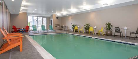 Una piscina interior con vista despejada al área de la piscina, rodeada de diferentes opciones de asientos, incluyendo sillas y mesas.