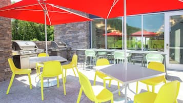 An outdoor patio with yellow chairs and tables, red umbrellas, and a stone wall.