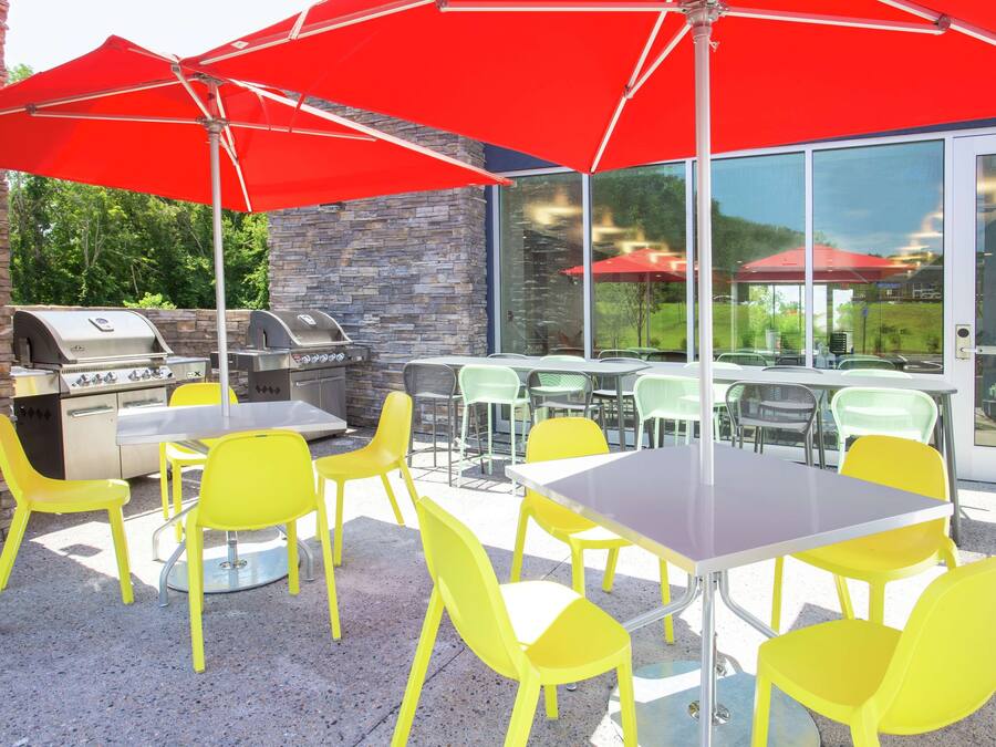 An outdoor patio with yellow chairs and tables, red umbrellas, and a stone wall.