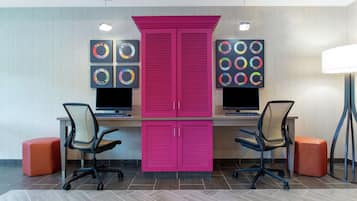 A modern office space with two desks, two chairs, a large pink cabinet, and artwork on the walls.