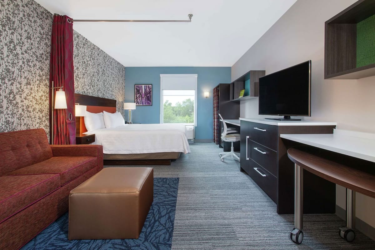 A hotel room with a bed, a desk, a television, a sofa, and a small table.