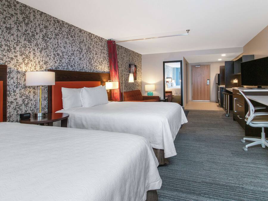 A hotel room with two beds, a desk, a TV, and a bathroom visible through an open door.