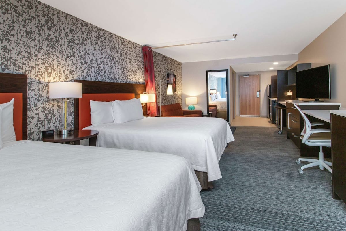 A hotel room with two beds, a desk, a TV, and a bathroom visible through an open door.