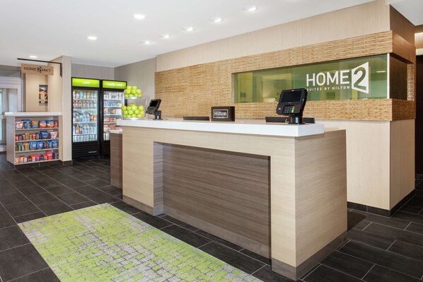 A hotel reception area with a counter, a digital kiosk, and a display of the hotel name.