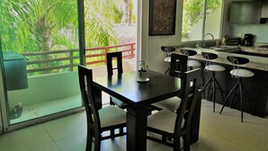 A kitchen with a dining area, a large window with a view of greenery, and a small island with bar stools. - Condo In Downtown of Playa del Carmen, four blocks to the 5th (Playa del Carmen)