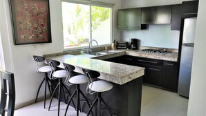 A modern kitchen with a granite countertop, black cabinets, a built-in stove, and bar stools. - Condo In Downtown of Playa del Carmen, four blocks to the 5th (Playa del Carmen)