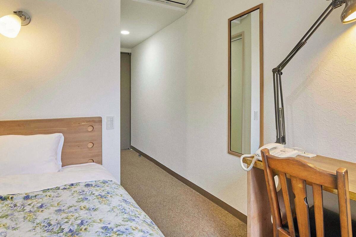 A hotel room with a wooden bed, a desk with a telephone, and a mirror on the wall.