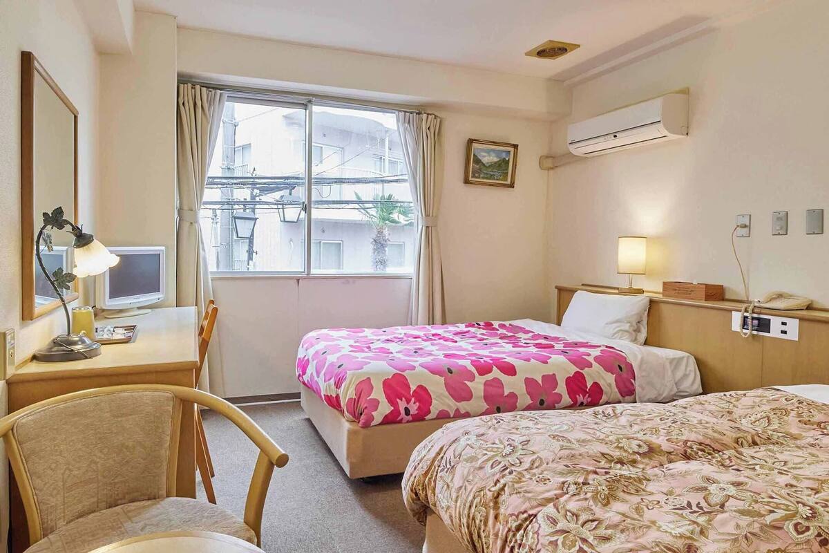 A hotel room with two beds, a desk with a computer, a chair, and a window with curtains.