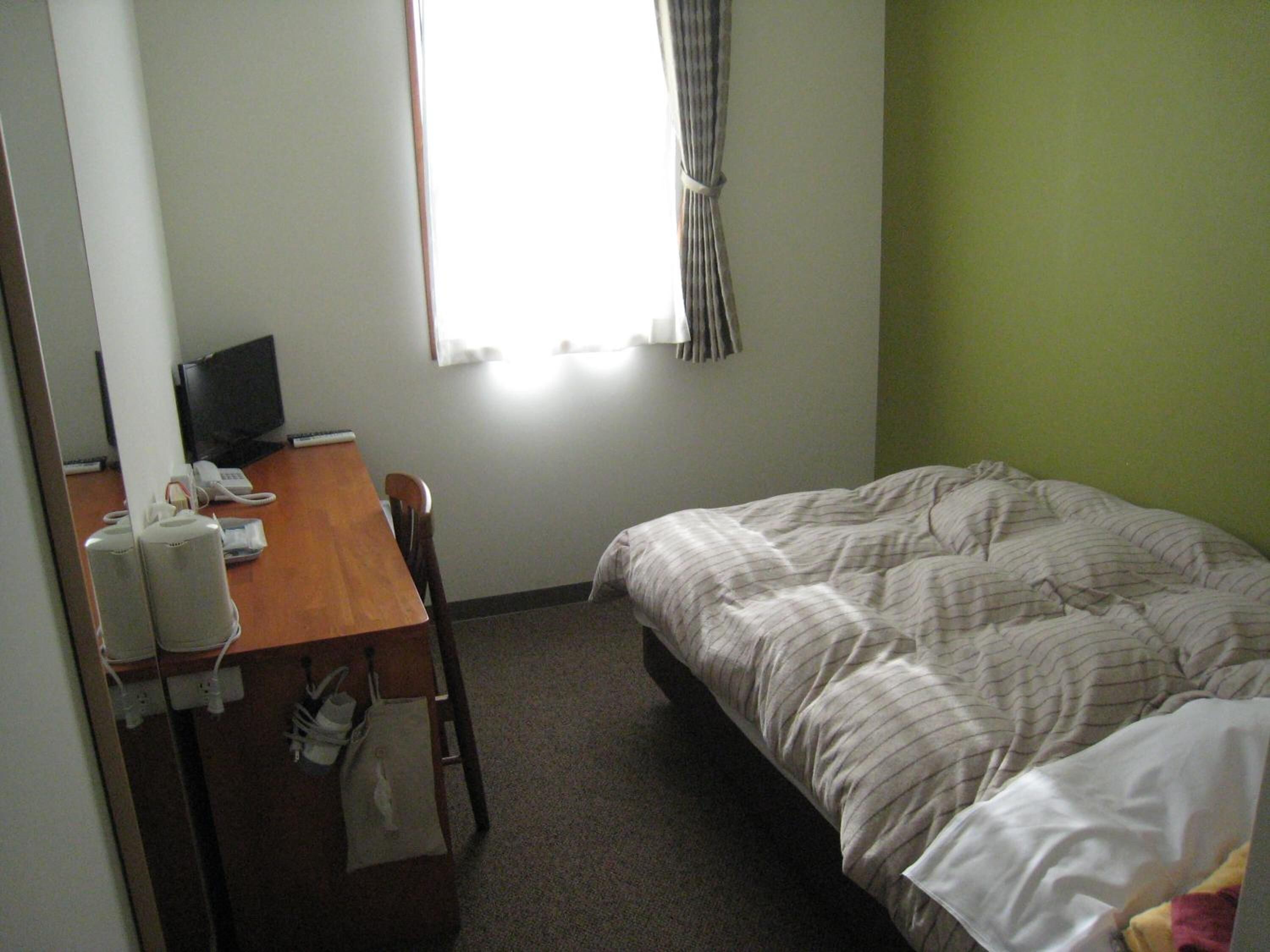 Een hotelkamer met een bed, een bureau met een computer en een raam met gordijnen.