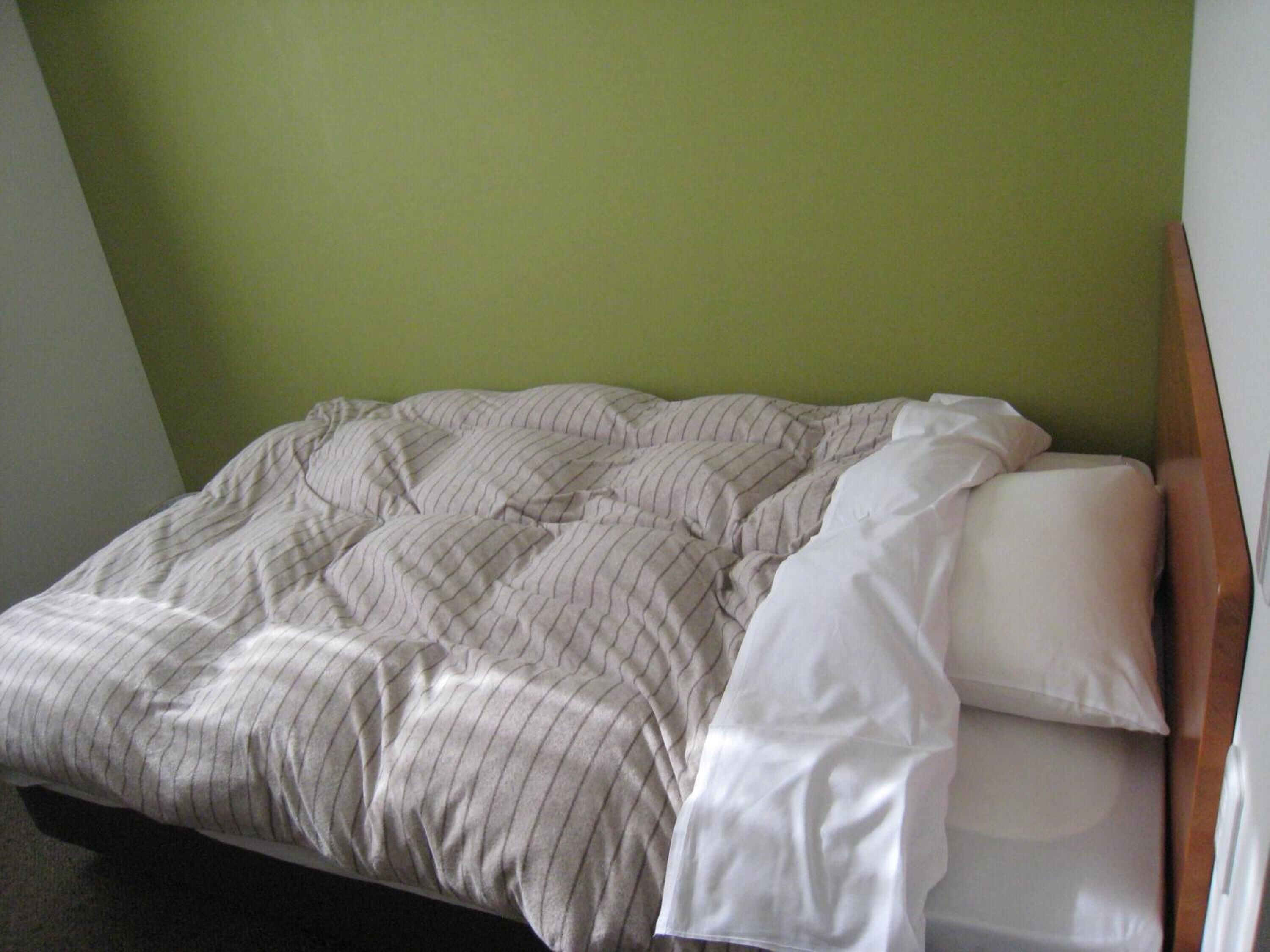 A bed with a striped comforter and white pillows in a room with green walls.
